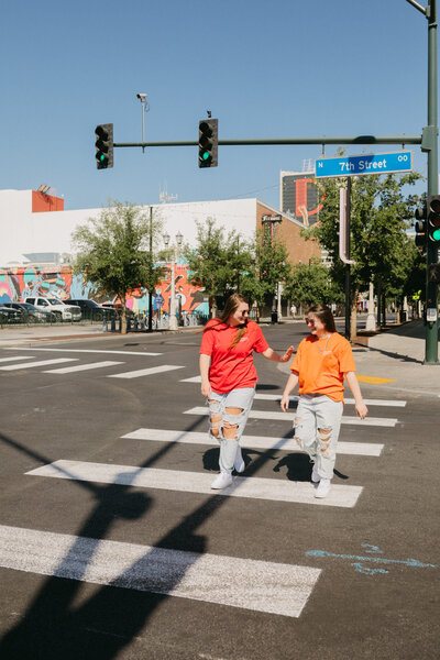 Two friends laughing and walking across a crosswalk.