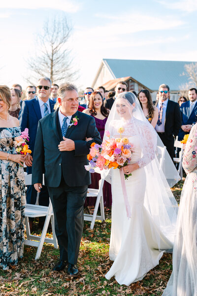 Bride and her dad walking down the aisle while guests smile around them