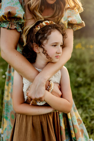 Photograph of little girl with curly hair and freckles getting hugged by mom from behind as she looks off in the distance by Overland Park Photographers.