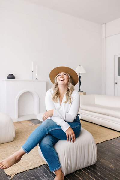 Realtor Leigh Kormos laughing and sitting on an off-white chair