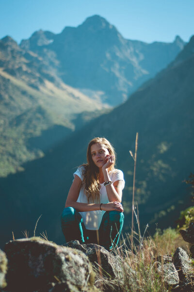Woman sits on rocks with mountains in the background on a sunny day,