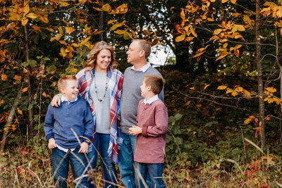 mom dad and two sons laughing with each other in a field during fall by Ashley Kalbus Photography