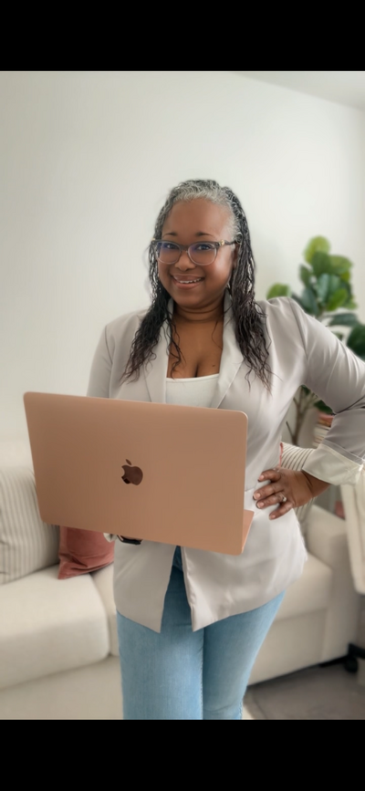Letitia Hopkins smiling confidently with hand on hip while holding her laptop in a blazer, embodying self-love, leadership, and Main Character Energy as Founder of Encourage Over Everything and life, love, and relationship coach empowering women into aligned, empowered lives and relationships.