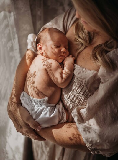 Fun with shadows, mother holding baby while sunlight creates lace shadows on baby's back