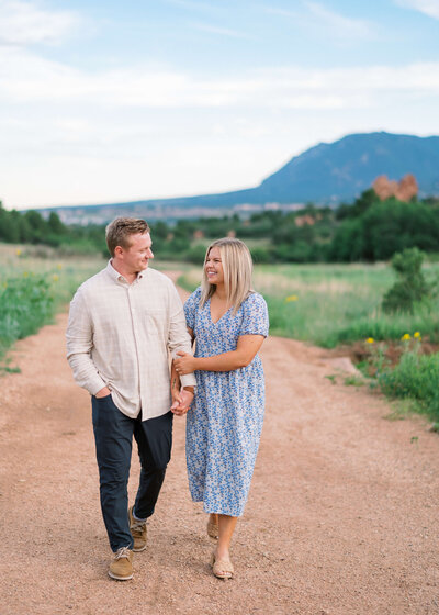 man and his blonde fiance walking on dirt path holding hands and smiling