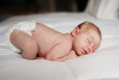 Newborn Photographer, a baby sleeps in a diaper on fresh linens