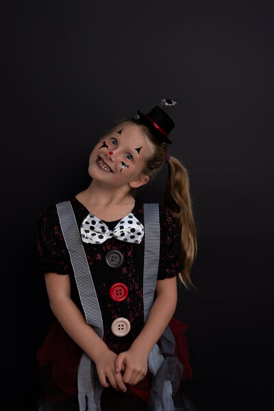 Young Girl wearing a creepy clown costume with a wild funny face in front of black backdrop. 