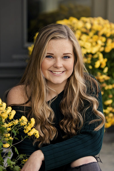 Senior girl smiling at camera with yellow flowers around her.
