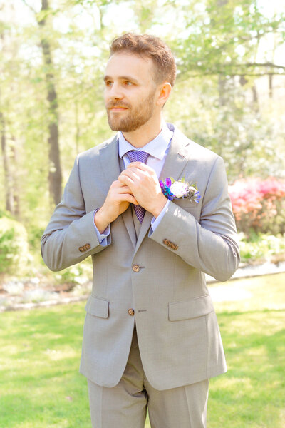 A dashing groom adjusts his tie before walking down the aisle with Gramercy Mansion Wedding Photographer in the gardens