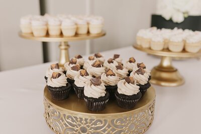 Photo shows a gold cake stand topped with mini cupcakes. The cupcakes are chocolate cake with peanut butter frosting. There's some other stands blurred in the background also containing different mini cupcakes.