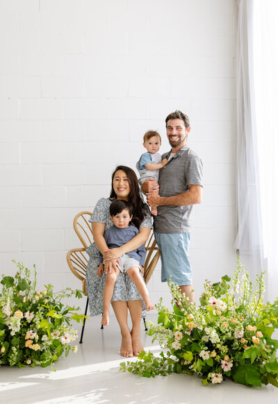 Family of 4 with small children posing in light and bright studio with green flower arrangements, photo by Anastasiya Photography - San Francisco Photographer