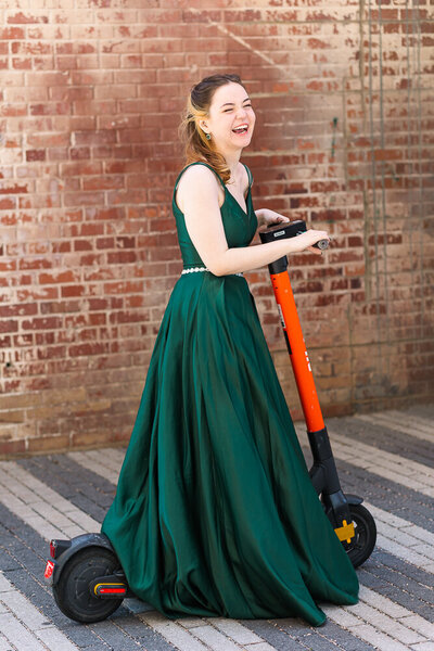 Prom photo session wearing long green dress standing in front of a red brick wall.