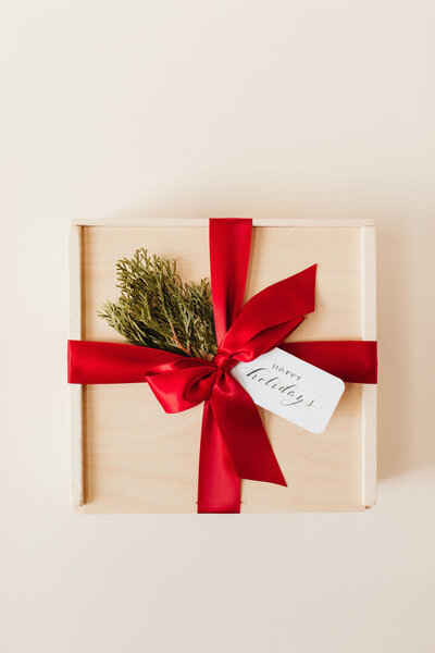 Pine gift box with red satin bow , juniper and custom happy holidays gift tag in calligraphy