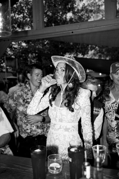 The bride turns up the fun at her after-party, sipping a drink in a playful cowboy hat—where wedding day elegance meets late-night revelry.