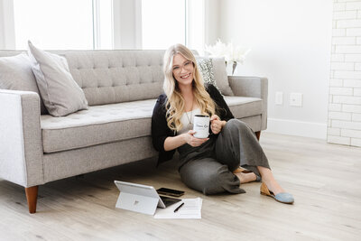 Realtor Tamara sitting in a pristine new construction home with a grey couch staged behind her