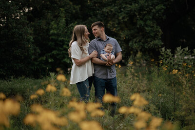 A family with a newborn baby poses in a field of yellow flowers at the South Carolina Statehouse gardens.