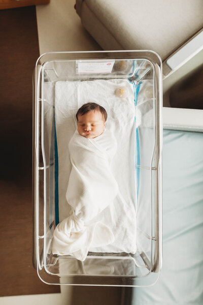 newborn baby swaddled in a white blanket in the hospital bassinet