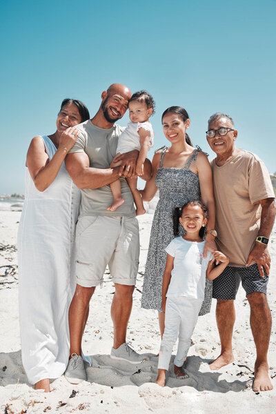 Multi-generational family smiling and posing together on a sunny beach.