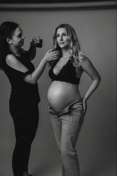 Hinter den Kulissen eines Schwangerschaftsshootings im Studio. Eine werdende Mutter wird von einer Stylistin für ihr luxuriöses Fotoshooting in Bamberg vorbereitet. Fotografiert von Cate Schmitt Portrait.