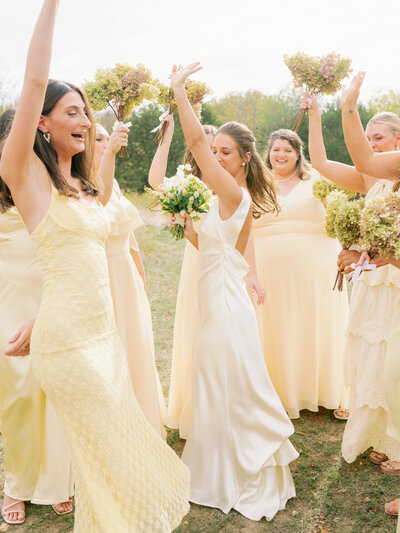 Bride and her bridesmaids all wearing yellow dresses smiling and holding their bouquets in the air