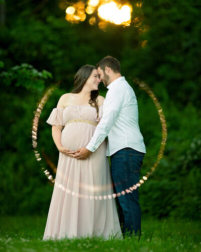 A pregnant woman and her husband look at each other in front of a sunset glow