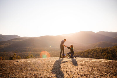 Young woman proposing to boyfriend on a viewing platform at a hike in Namadgi National Park near Canberra ACT. Photography by Acacia & Grace Photography