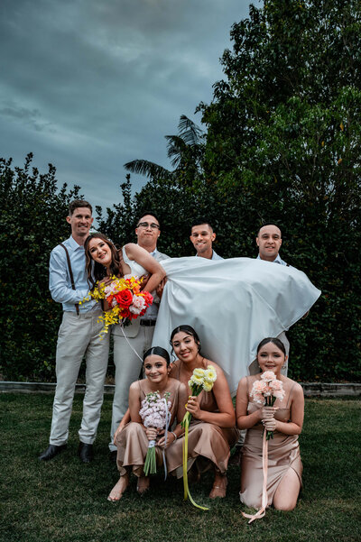 A joyful wedding party poses together for a photo in front of a beautiful tree, capturing a moment of celebration.