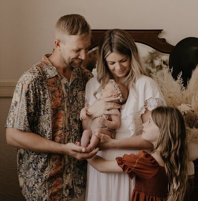 Close up of Kaz, wearing metal framed sunglasses and a black top, with her daughter on her back.  Kaz is smiling, her daughter has a very cute grumpy expression.