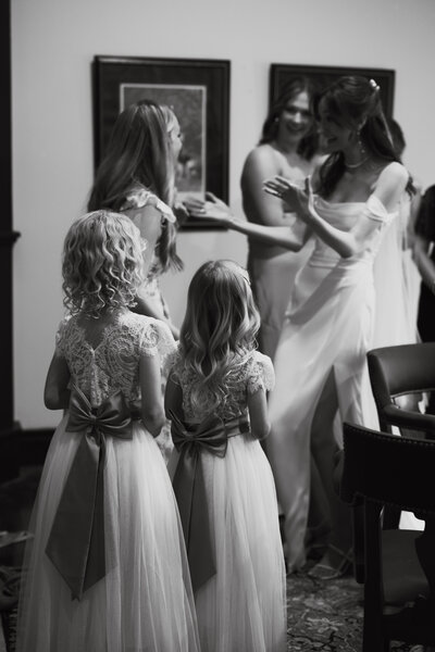 bride hugs friend as flower girls watch