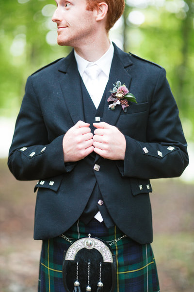 scottish groom wearing a kilt shows off his textural boutonniere by roots floral design