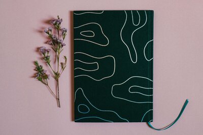 Plain background featuring dried flower and dark planner with swirled design