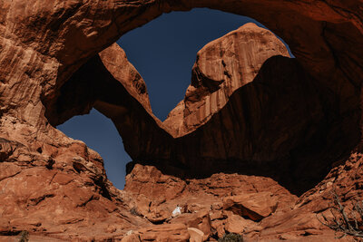Wedding couple standing under double arch in their elopement in Moab, Utah
