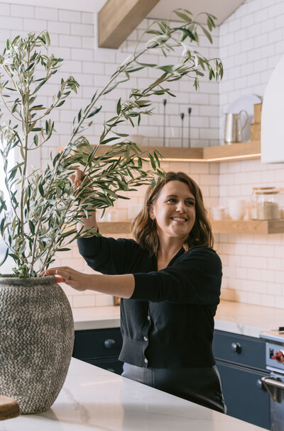 woman posing in kitchen plaster hood dark cabinets blue cabinets subway tile subway backsplash pot filler island large branches in vase