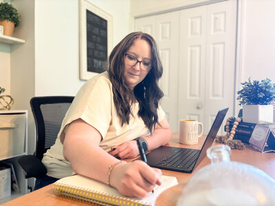 Ali jotting down notes in a spiral notebook while working from her organized home office