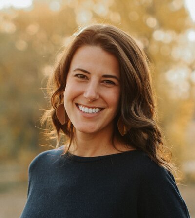 A woman with long hair wearing a blue shirt smiles warmly in Littleton, Colorado.