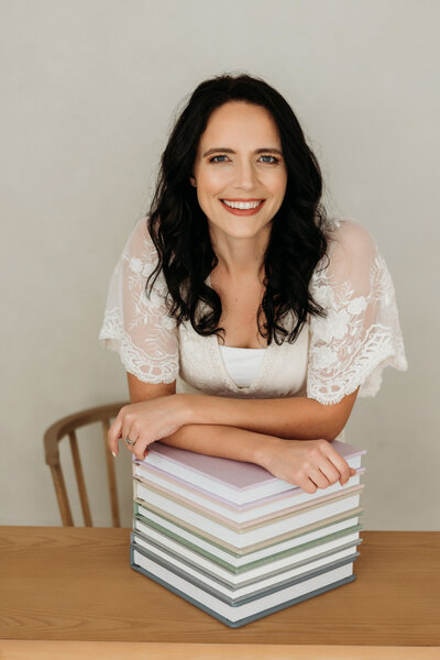 photographer, Alyson Berg, smiles for portrait with stack of photo albums
