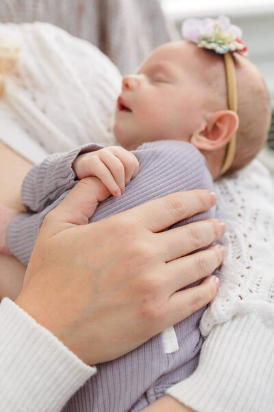 A newborn girl in her Alexandria home snuggling with mom and holding her thumb in her hand.