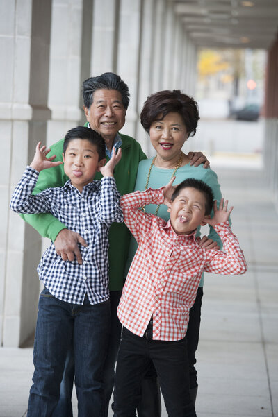 Two small kids smiling and making funny faces with their parents standing behind them 