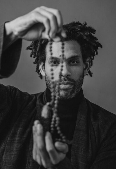 A person holding up a beaded necklace in front of their face 