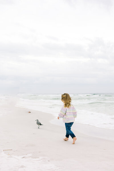 Little girl photographed trying to chase a bird on the beach.