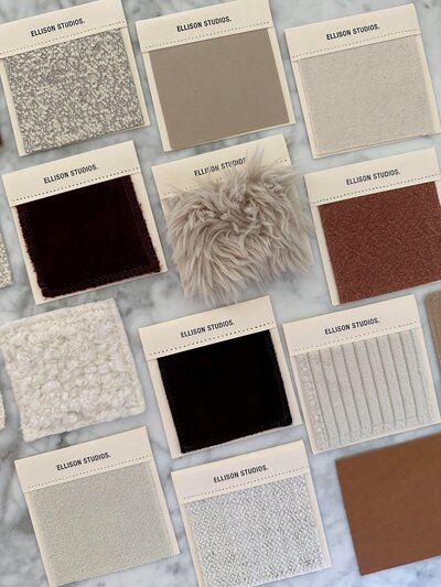 A curated selection of fabric samples from Ellison Studios, including linen, velvet, boucle, teddy, and leather, displayed on a marble table for design inspiration and texture exploration.