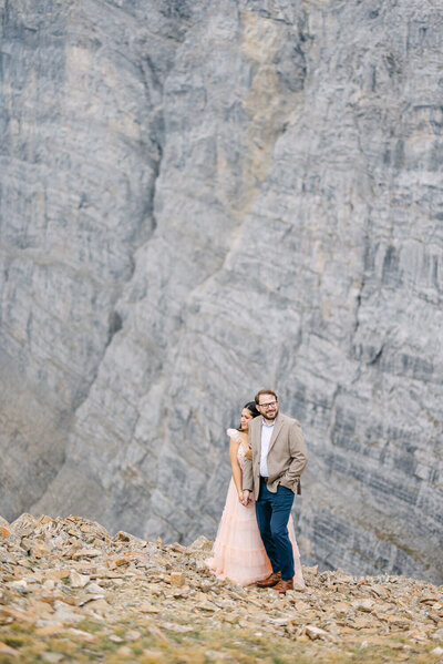 Engaged couple at the summit of Ha Ling Peak and Miners Peak in Canmore Alberta after a mountain adventure session surrounded by stunning Rocky Mountain views
