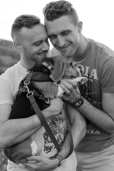 black and white photo of couple hugging their dogs