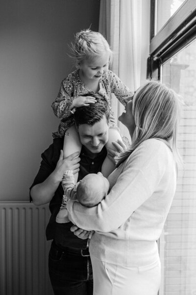 Vader en moeder houden pasgeboren baby vast terwijl dochtertje in de nek van papa zit