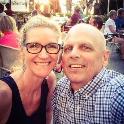 Phillipa Leseberg with glasses and Eric Leseberg in a checkered shirt smile outdoors, with a crowd in the background, capturing a moment that feels straight out of Phillipa Leseberg's memoir.