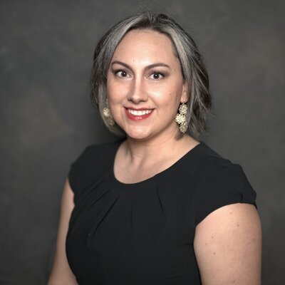 Photo of a woman wearing large earrings, and a black shirt, in a professional setting with a black and grey background.