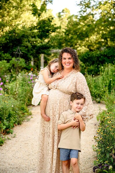 Charlotte area mother holds her daughter against her pregnant belly with her arm around her son in a private flower garden venue