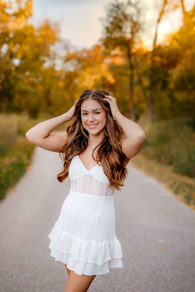 A beautiful brunette high school senior posed on the grass laying on her belly on a white dress at Cliff Cave Park.