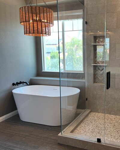 A large black soaking tub in a remodeled bathroom with hexagon black tiles, a white vanity, and subway tiled shower.