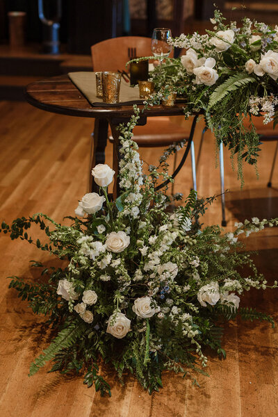 Large ground floral piece with white roses, greenery, and wild foliage